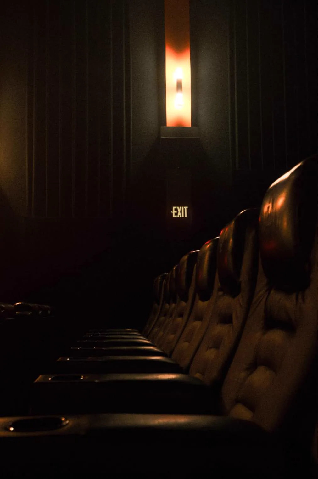 Empty cinema seats beneath a glowing wall light and an exit sign